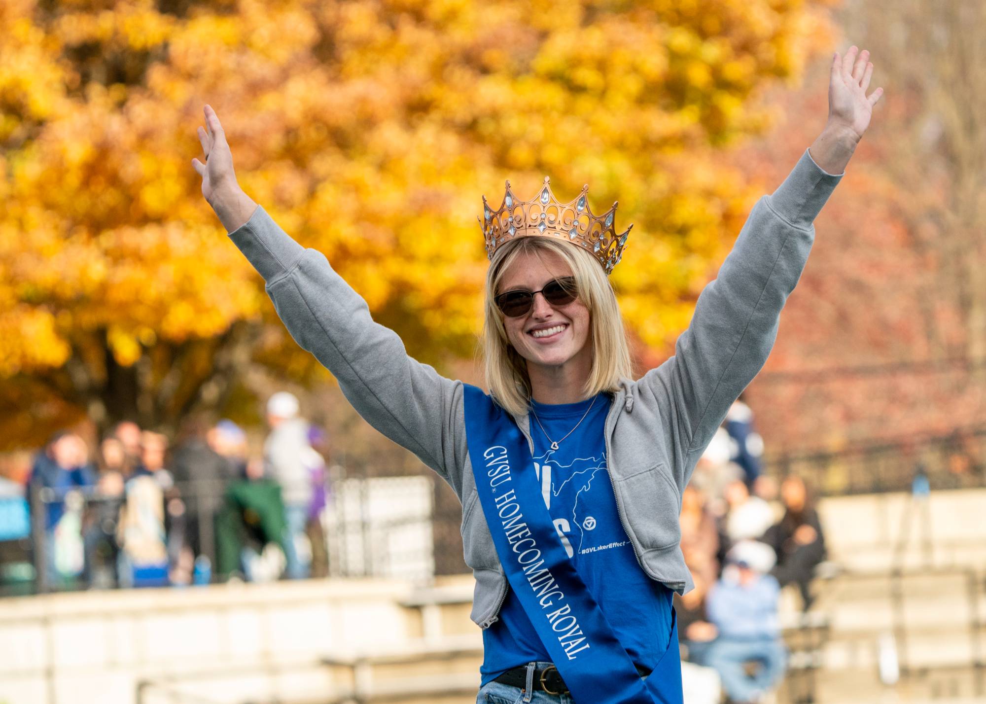 female student wearing crown waving to people outdoors